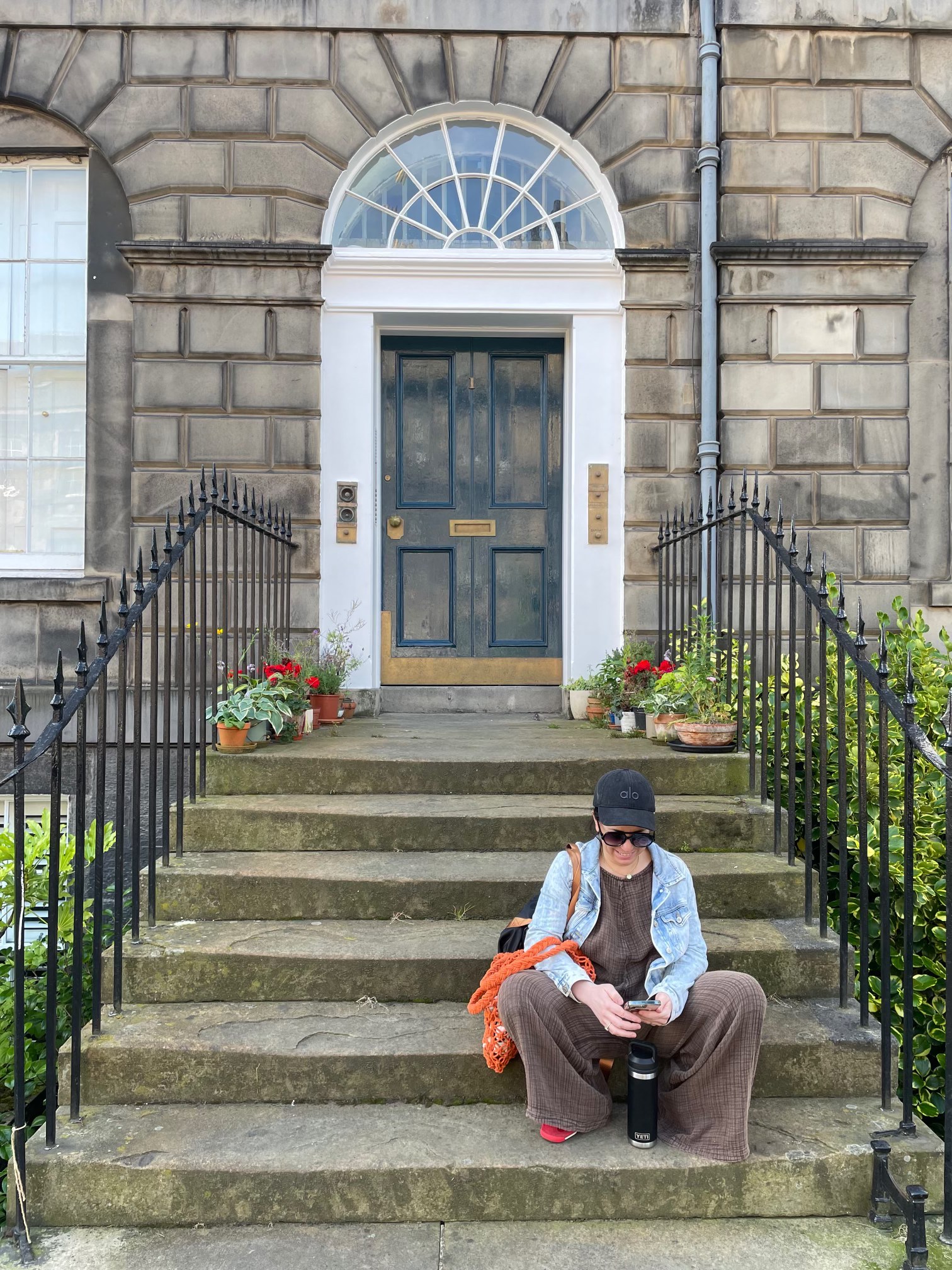 Marylou seated on stone steps beneath a welcoming doorway, surrounded by plants.